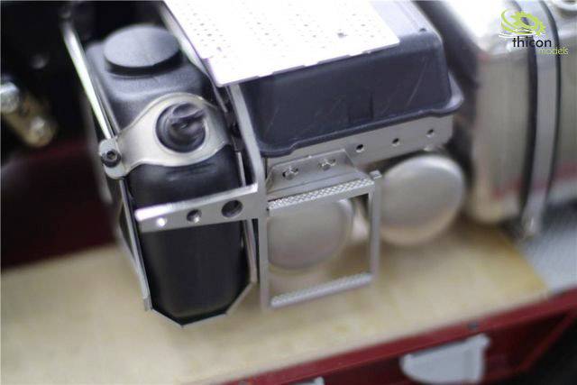 Close-up of a mechanical component with a black container and a metal frame. A logo is visible in the top left corner.