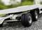 Close-up of a model vehicle trailer with black tyres on a gravel surface, background slightly blurred.