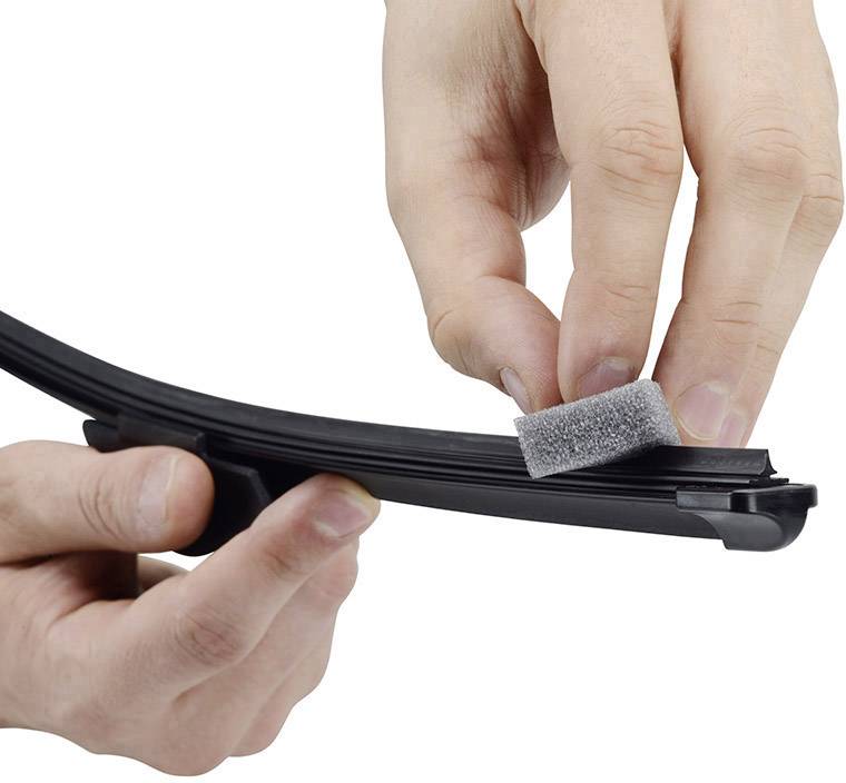 Hand cleans windscreen wiper with grey foam pad.