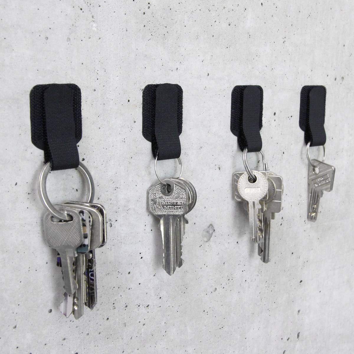 Four bunches of keys with various keys hang side by side on a concrete wall from black hooks.