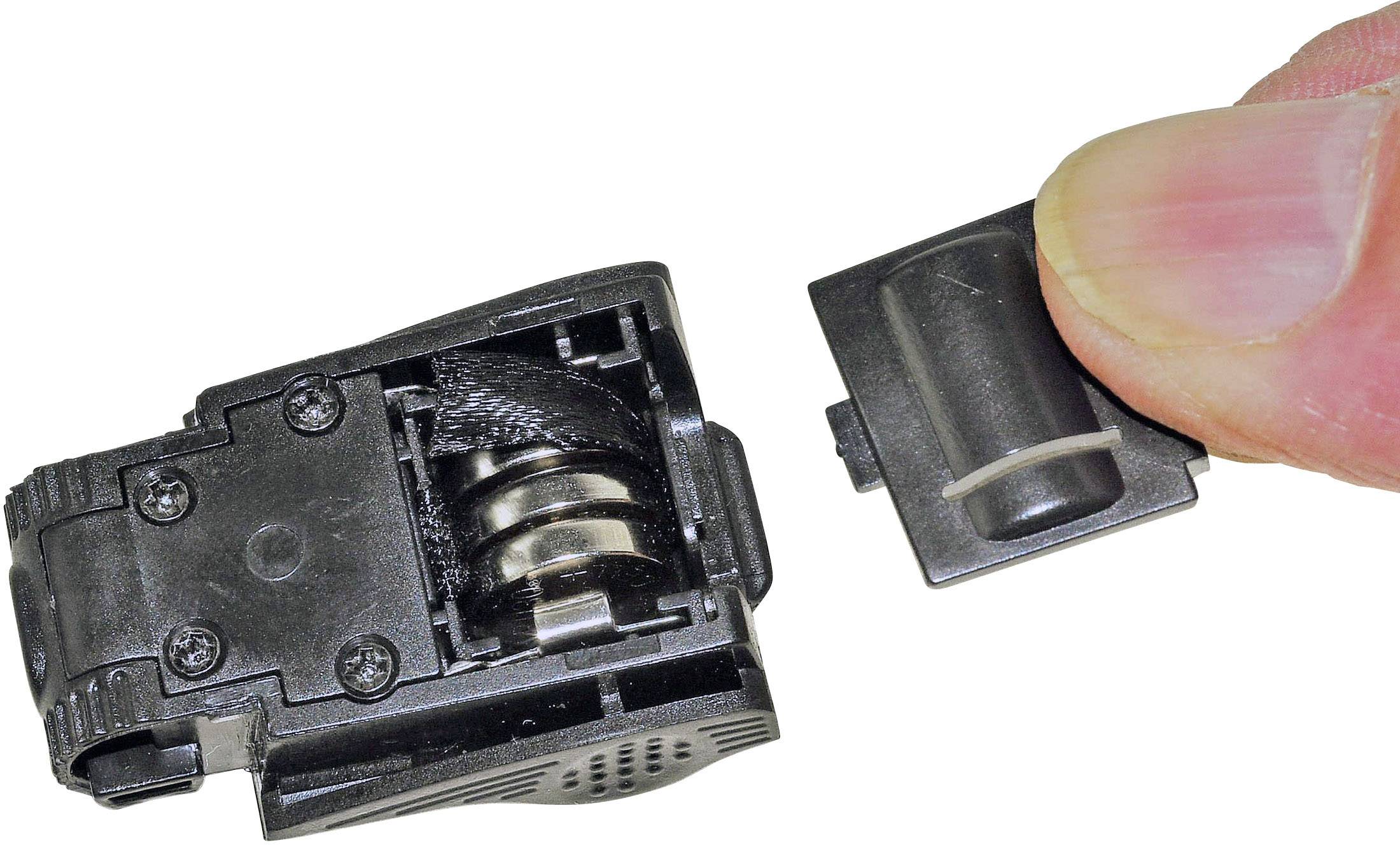 A hand holding a small black mechanical device with a removed cover revealing internal coils.