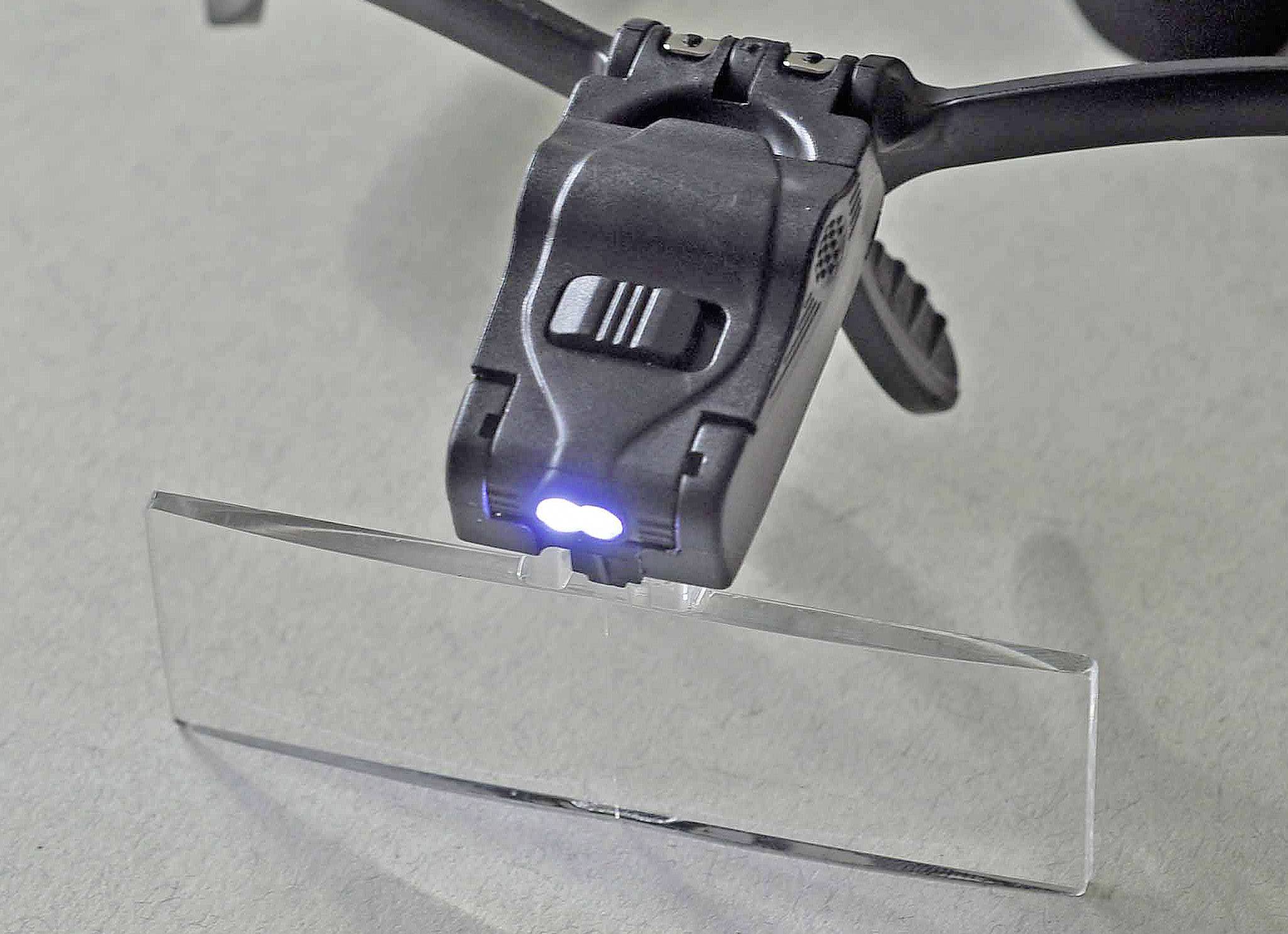 A magnifying glasses with integrated LED lighting lies on a table. The lamp is switched on and illuminating the lens.