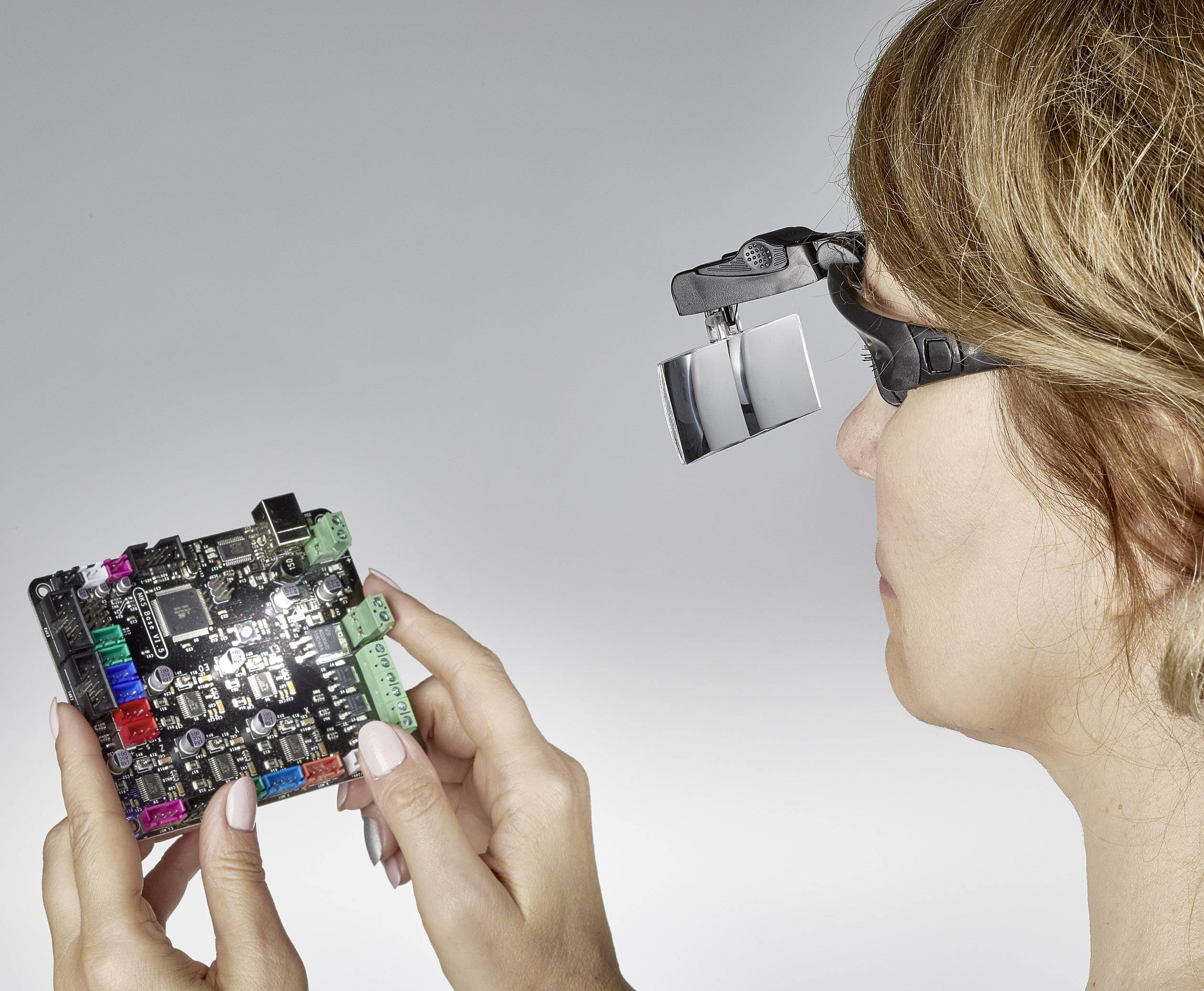 A person is examining a circuit board through magnifying lenses. They are inspecting the details of the circuit.