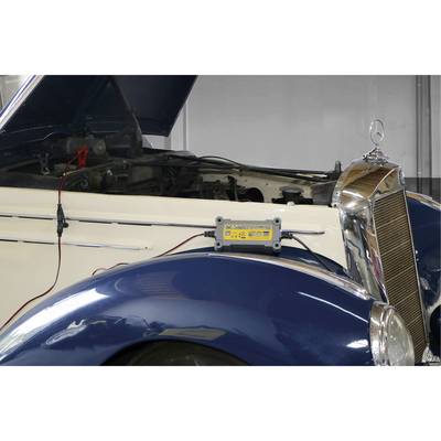 An old car with an open bonnet is being charged with a charging device.