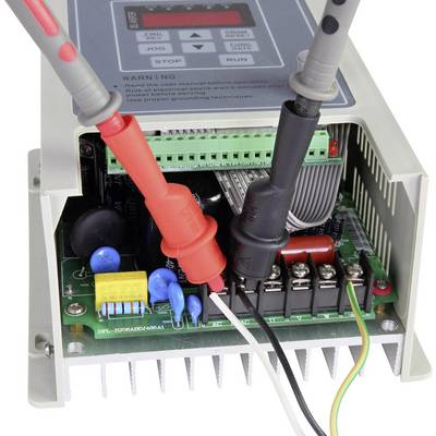 An opened electronic device with visible circuit boards and two connected test leads (red and black).