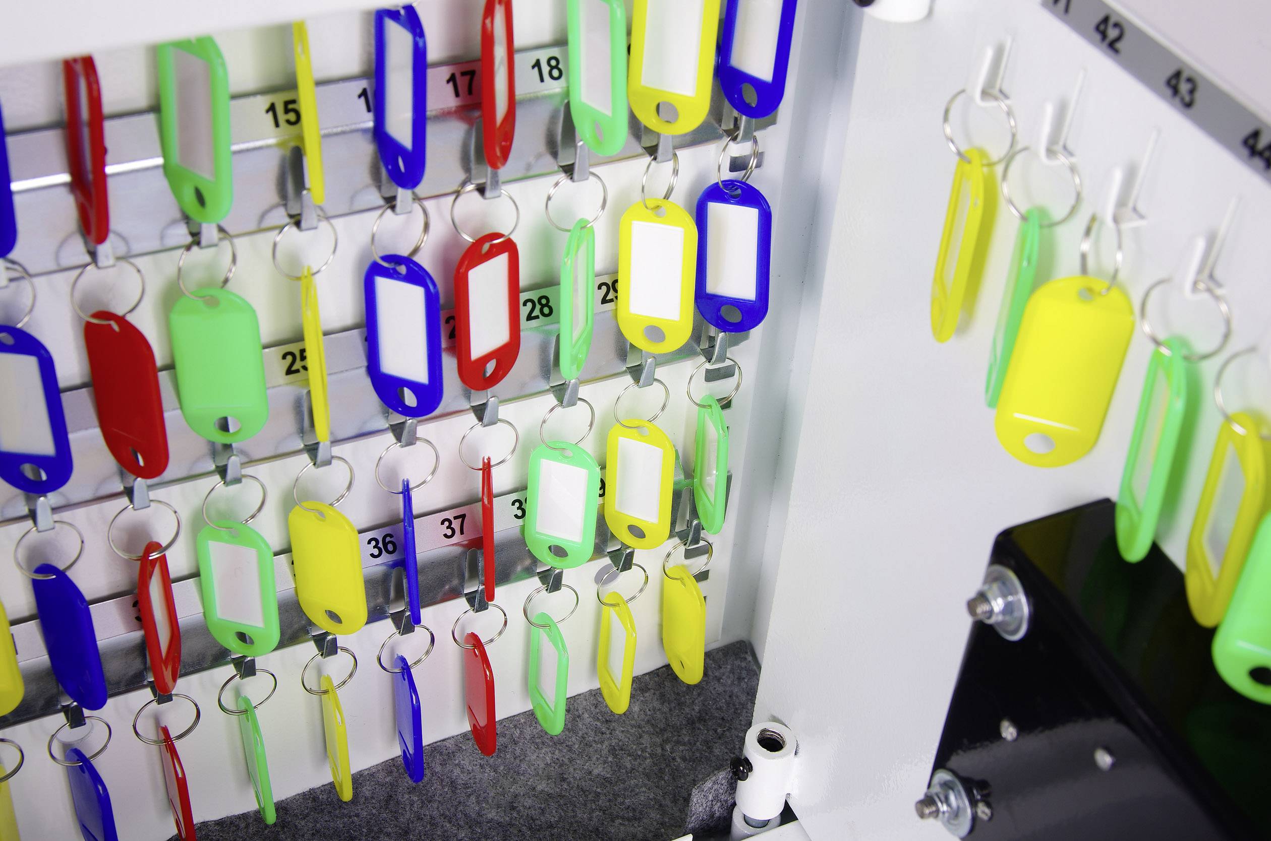Several colourful key fobs hang on numbered hooks in a key cabinet.