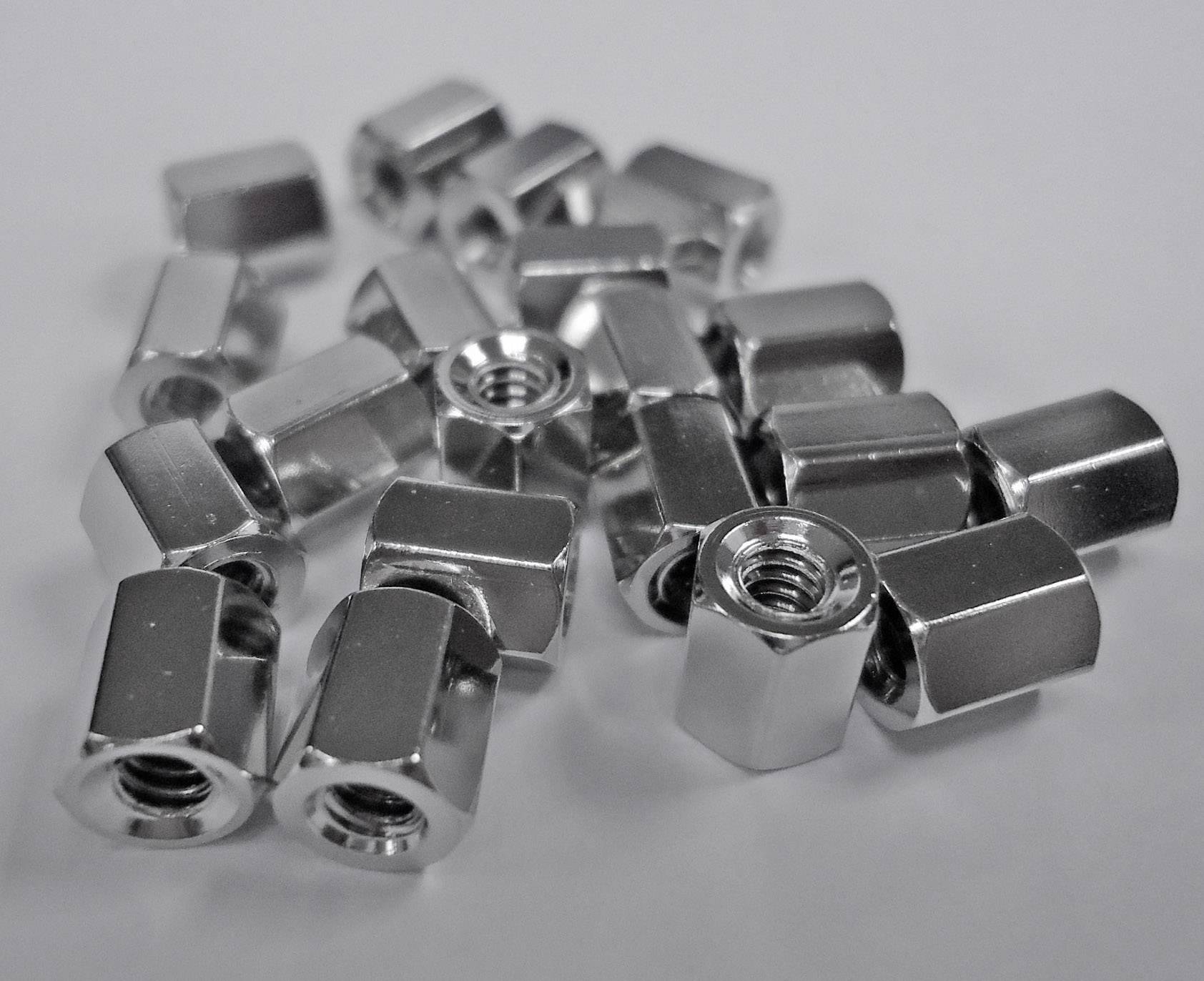 Several silver, hexagonal nuts are unevenly distributed on a white surface.