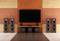 Home cinema setup with a large flat-screen television, four floor-standing speakers, and three subwoofers in front of an orange-brown wall.