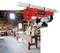 A red electric winch hangs in a workshop with wooden workbenches and tools.