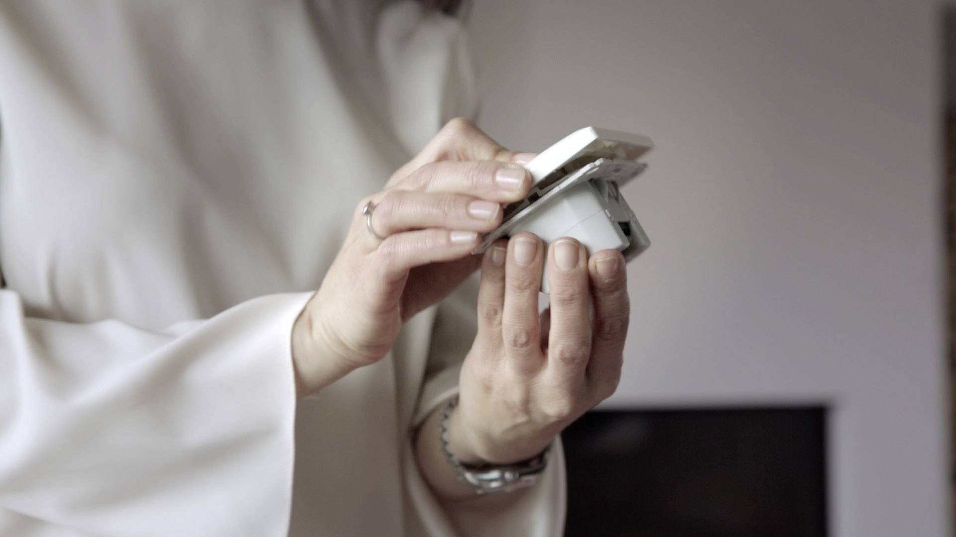 A person is holding a socket cover and preparing it for installation. They are wearing light-coloured clothing.