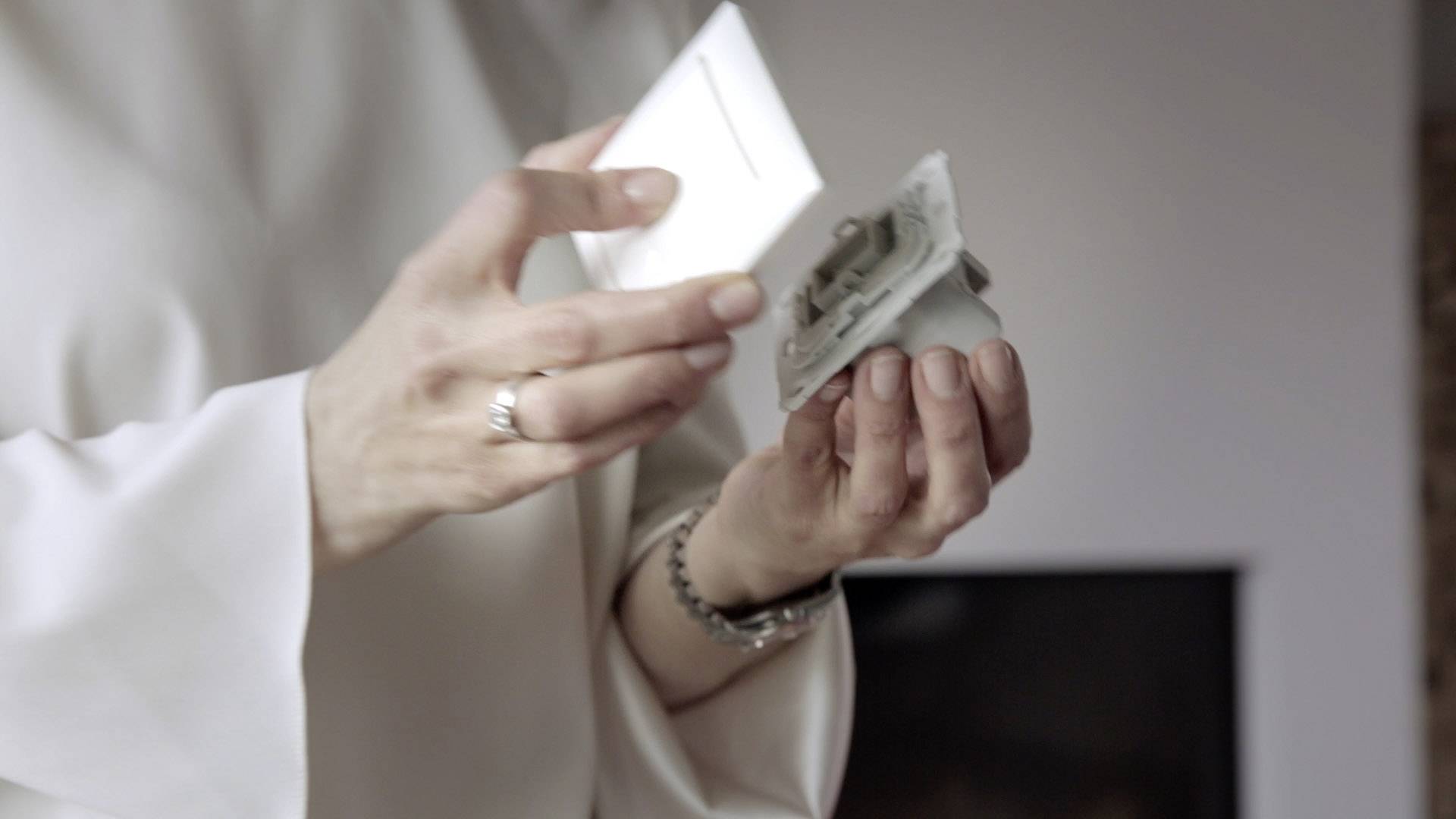 A person is holding a light switch and installing it. A blurred interior space is visible in the background.