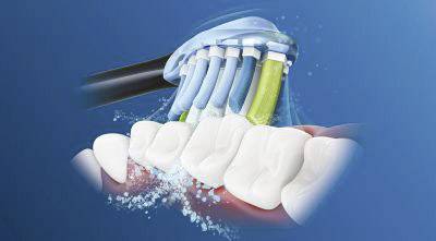 A toothbrush with colourful bristles cleans teeth with foam on a blue background. The illustration demonstrates the movements of the bristles.
