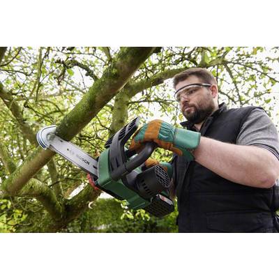 A man wearing safety glasses and gloves is sawing a branch off a tree with a cordless chainsaw.