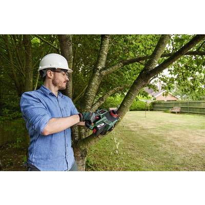 A man wearing a safety helmet is cutting branches of a tree with a handheld chainsaw in a garden.