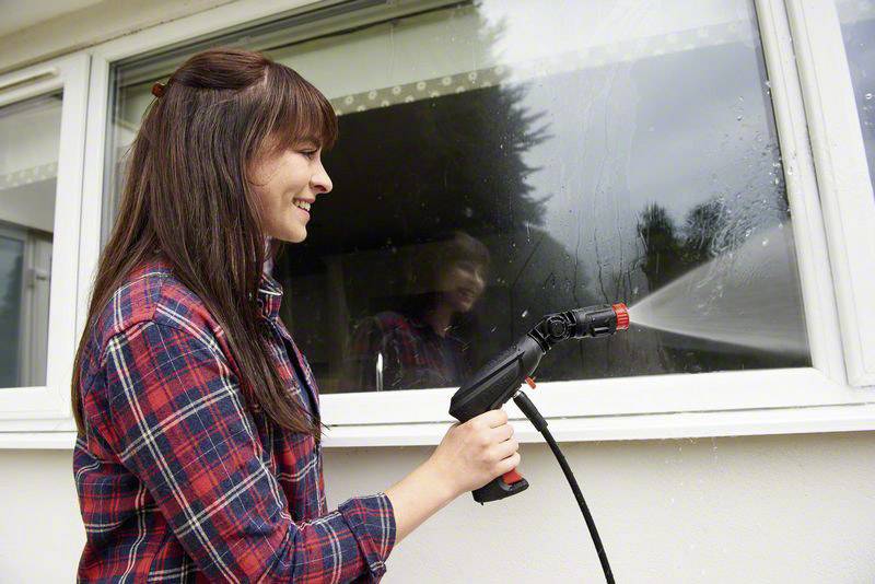 A woman in a checked shirt sprays water onto a window.