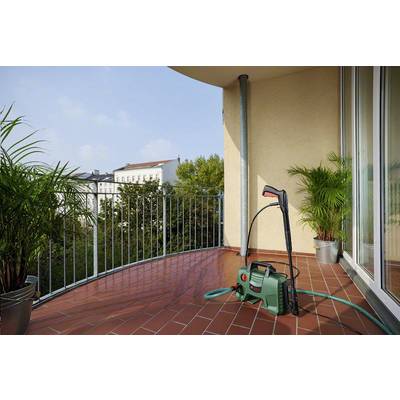 'Green pressure washer on a balcony with a view of buildings and trees. Potted plants are positioned on the left and right.'