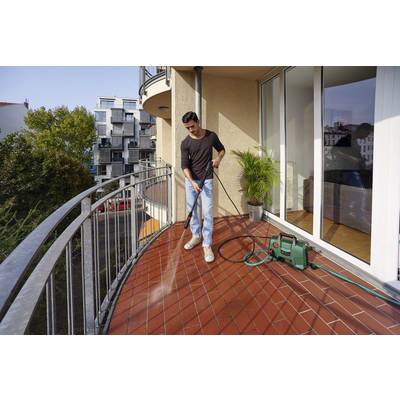 A person is cleaning the balcony floor with a pressure washer during the day, with modern residential buildings in the background.
