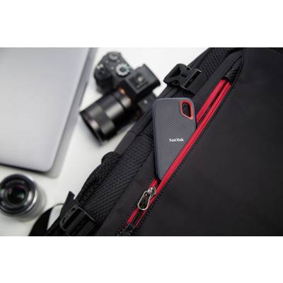 A portable SanDisk hard drive is tucked into the outer pocket of a black rucksack. A camera and laptop can be seen in the background.