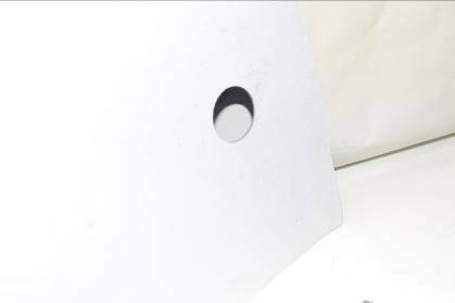 A circular hole in a white angled surface, with a beige area in the background.