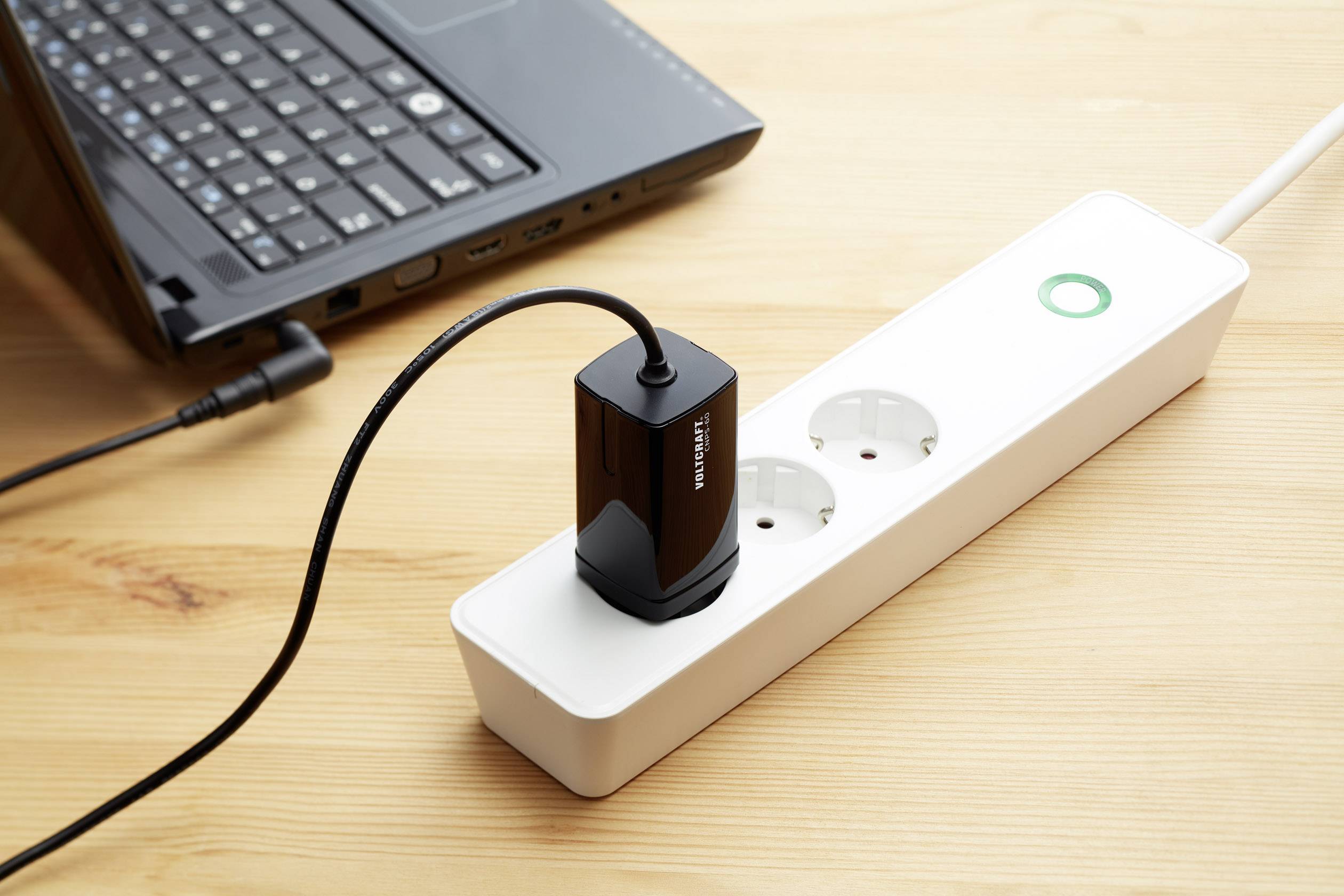 'A laptop is connected to a white extension socket. The extension socket has three outlets, one of which is in use.'