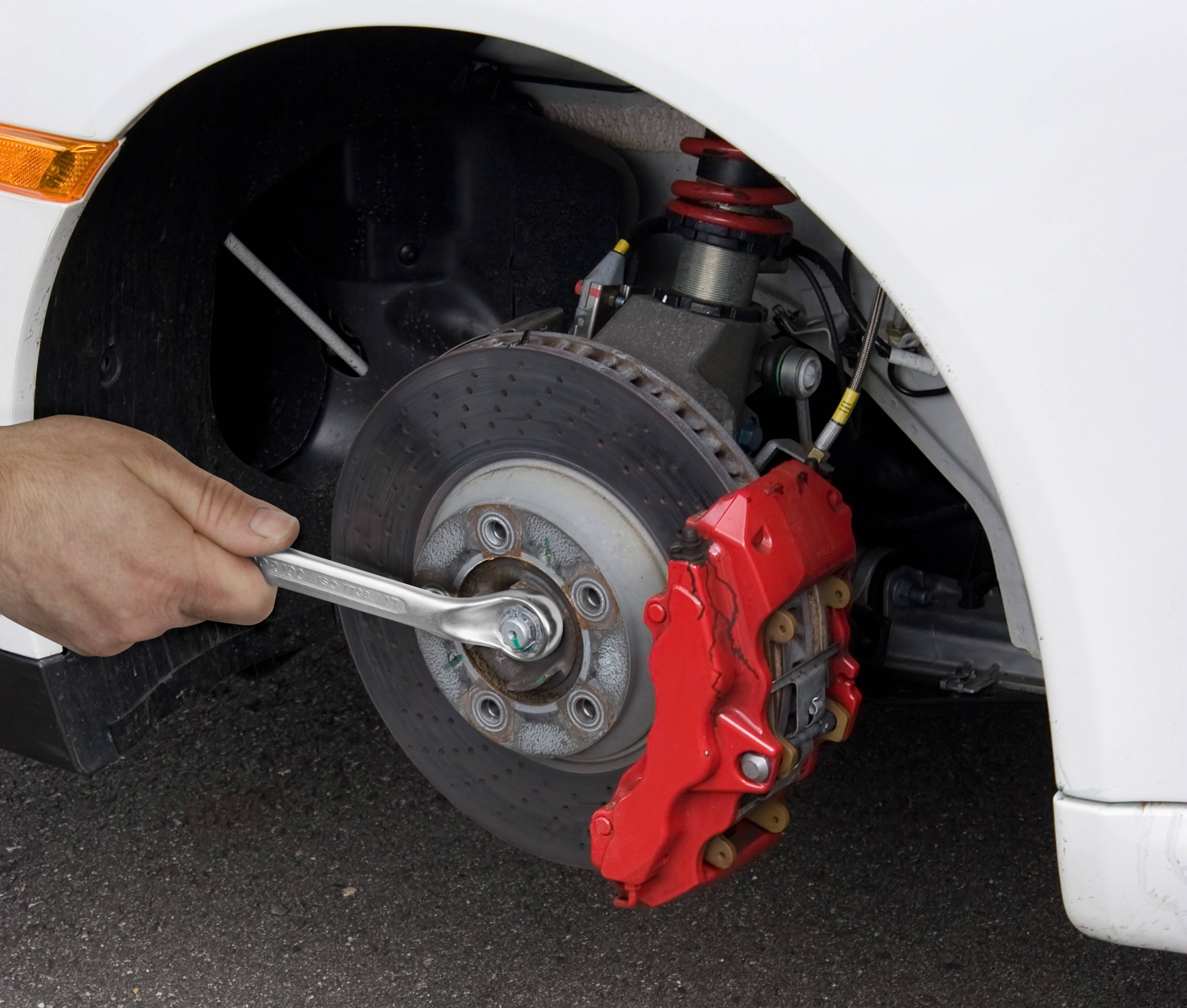 A hand tightens the wheel nut of a car with a spanner. The red brake calliper cover is clearly visible.