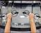 Two hands are holding a car windscreen with suction cups. The scene depicts the installation or replacement of the windscreen in a workshop.