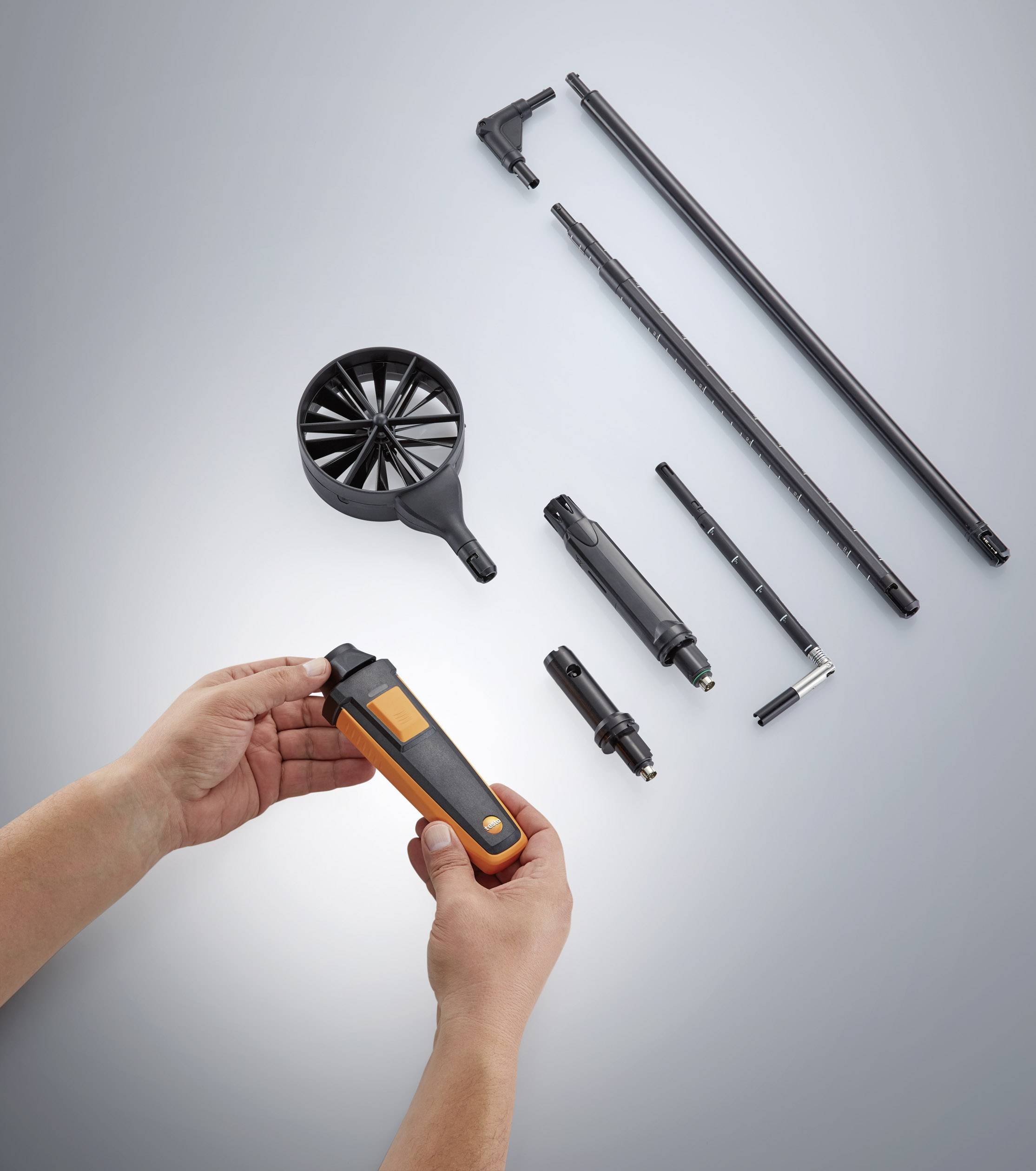 Some measuring instruments and accessories are lying on a table. Two hands are holding an orange, hand-sized device, ready for use.