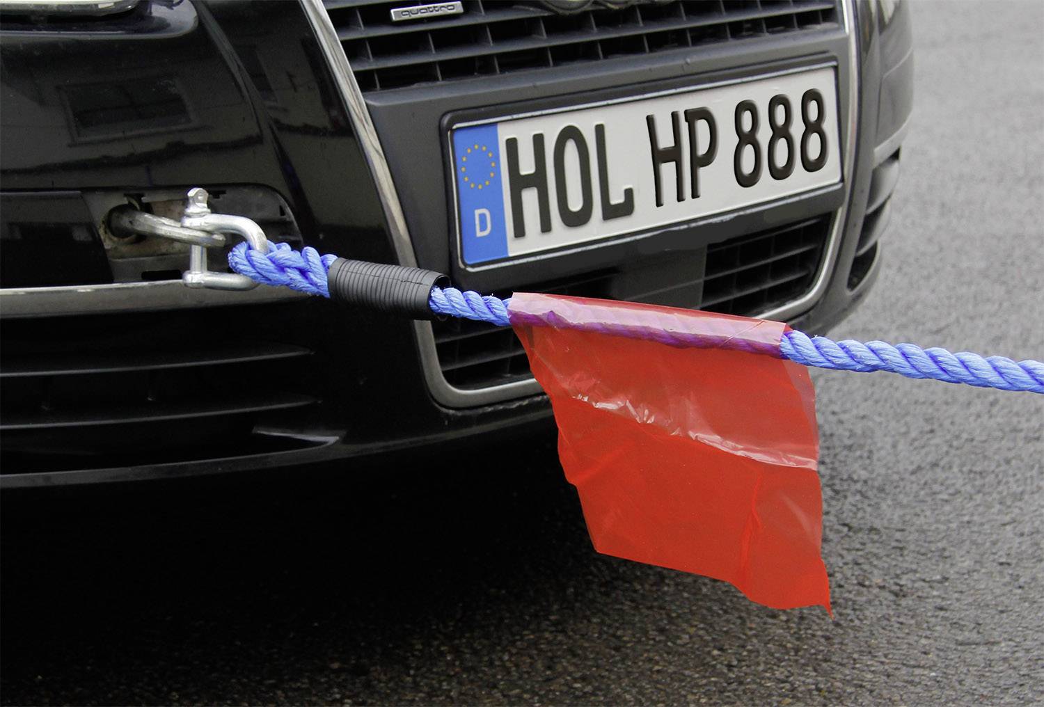 A car is being towed by a blue towing rope with a red flag, attached to the front towing hook.