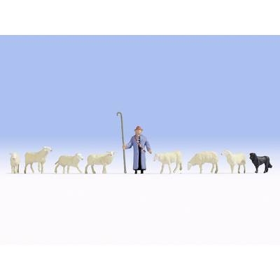 A shepherd in blue clothing and a hat stands with a sheepdog and seven sheep on an open field under a clear sky.