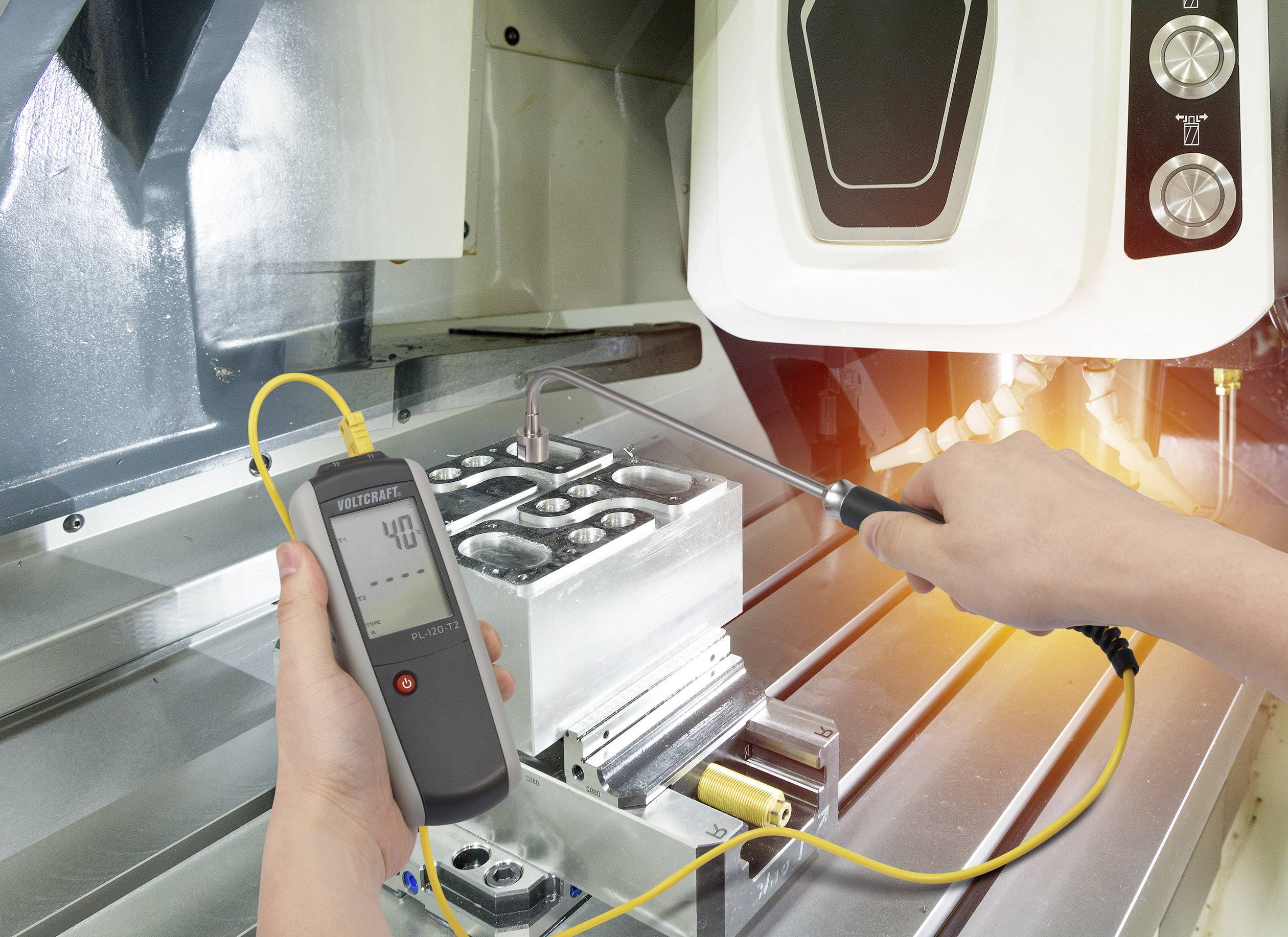 A person is measuring the temperature of a metal component in an industrial environment using a digital thermometer.