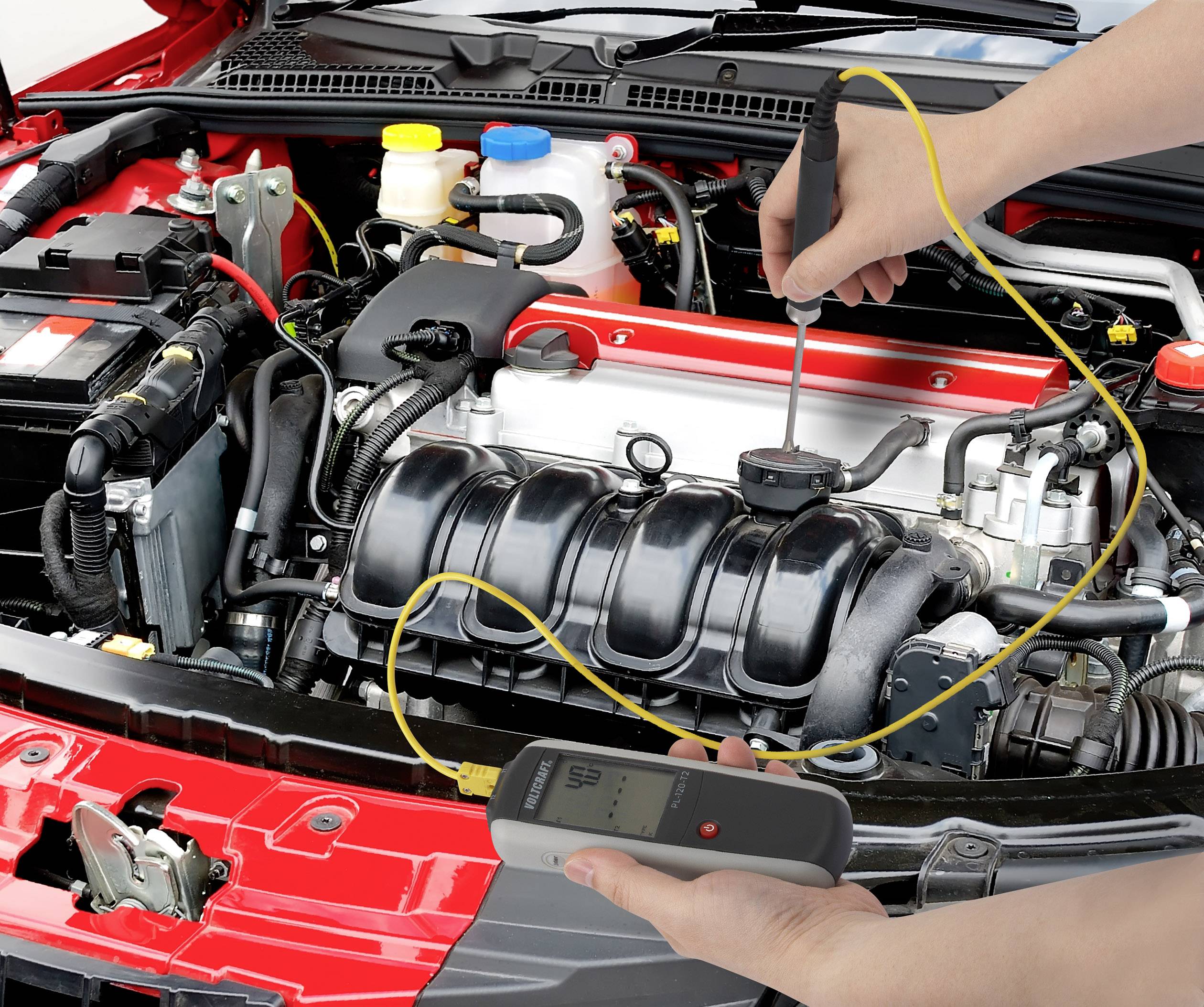 A person is measuring the voltage of the car battery under the open bonnet of a car using an electronic device.