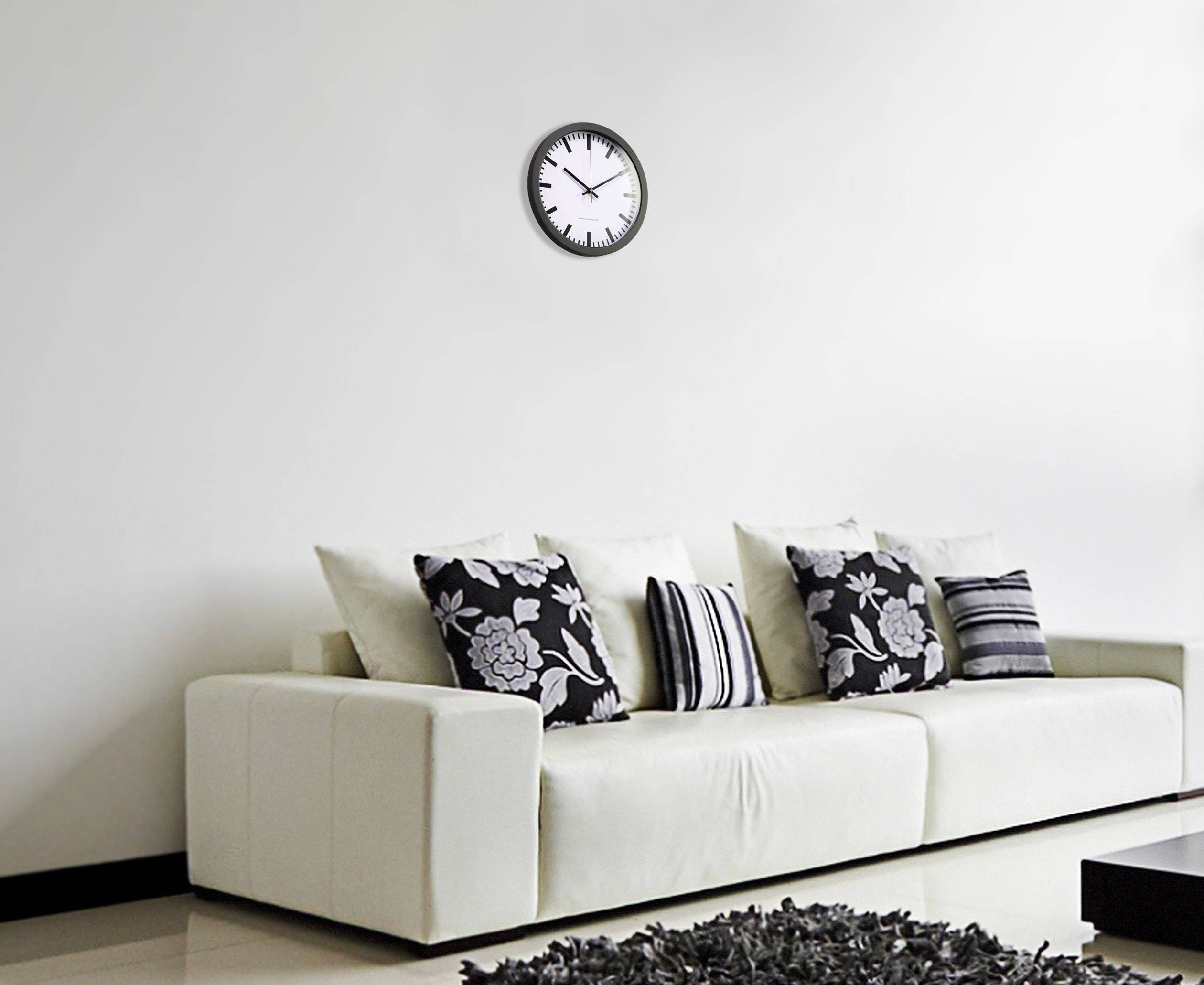 A white sofa with black and white patterned cushions stands in front of a white wall. An analogue clock hangs on the wall.
