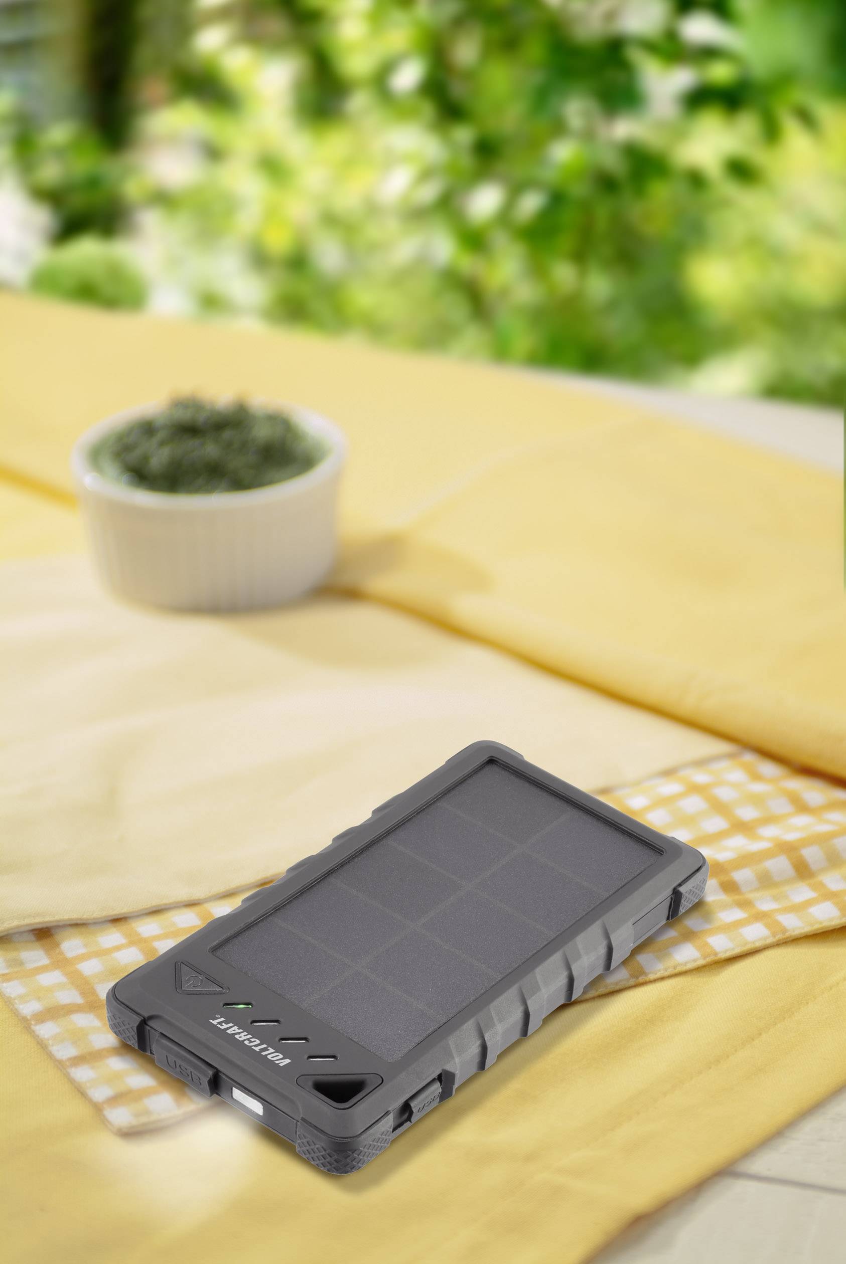 A robust, grey solar charger lies on a table with a yellow cloth. Blurred green is visible in the background.