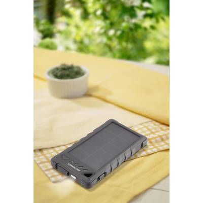 A robust, grey solar charger lies on a table with a yellow cloth. Blurred green is visible in the background.