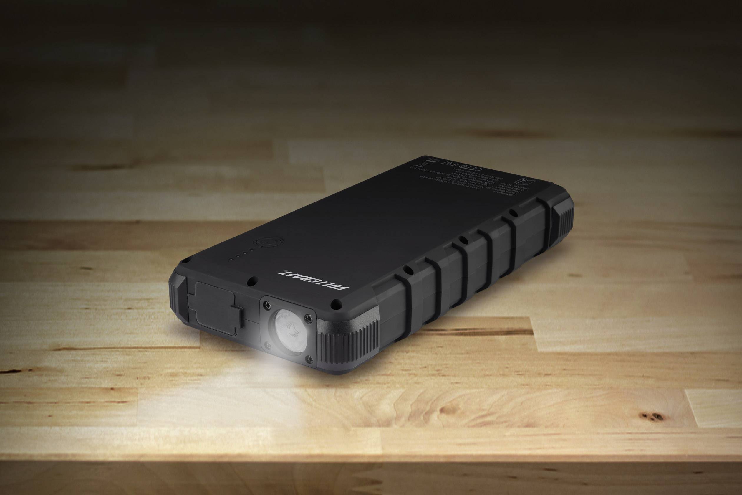 Black, compact power bank with robust construction and torch function, resting on a wooden table.