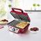 A red waffle maker on a kitchen worktop. To the left, a plate with a waffle, to the right a bowl of cherries. Bright, modern kitchen.