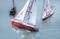 Three model sailing boats with white sails and red hulls sailing on calm water. The sails are marked with 'Atlantis'.