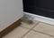 'Mousetrap placed behind a cupboard on tiled flooring, ready for pest control in a domestic setting.'