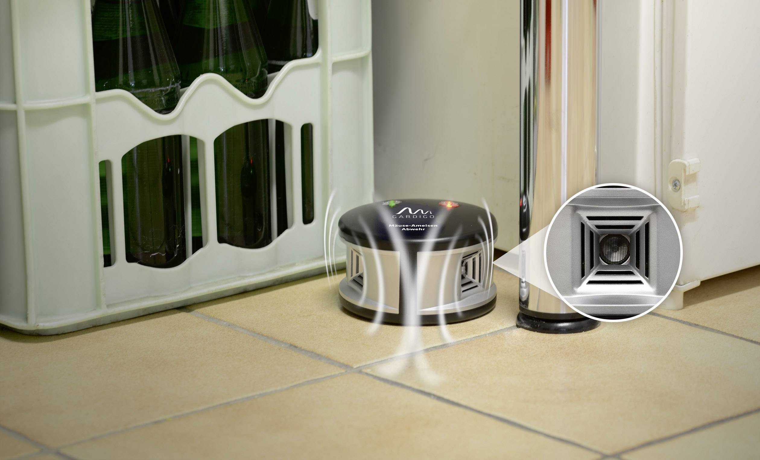 A marten deterrent device stands on a tiled floor next to a box of bottles and a door, designed to ward off vermin.