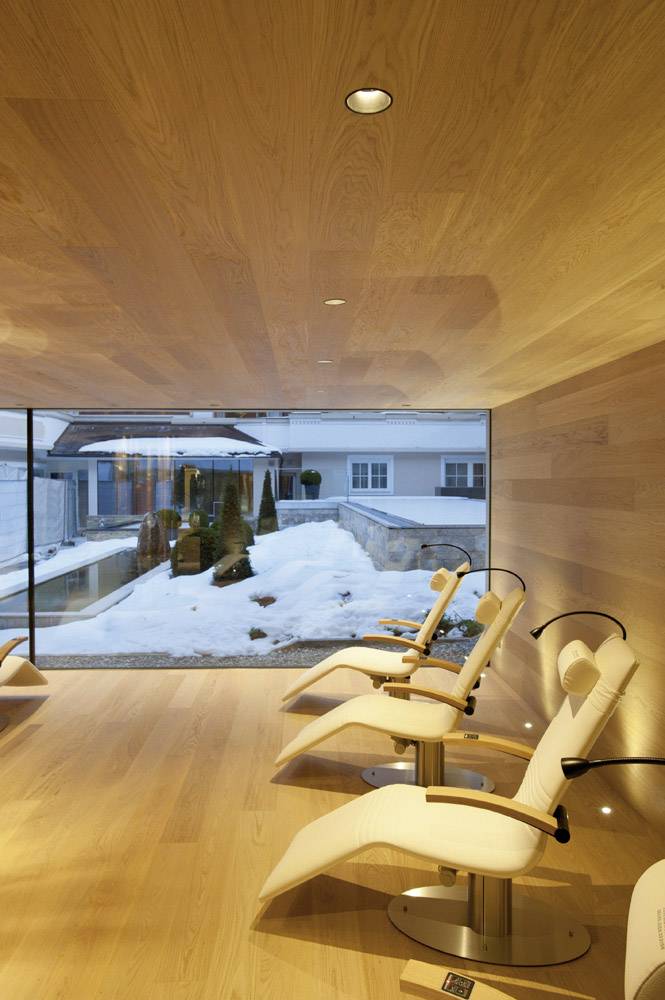 A modern room with a wooden ceiling and wooden floor offers bright chairs with a view of a snow-covered landscape through a large window.