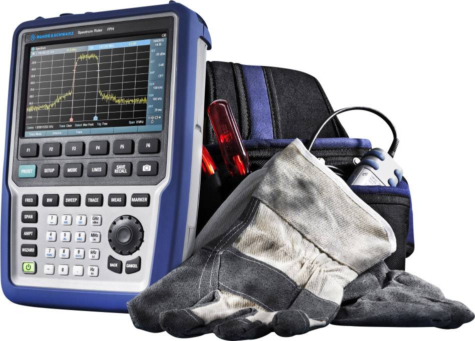 Portable spectrum analyser with colour display showing frequency measurement. Beside it are dirty work gloves and a tool bag.