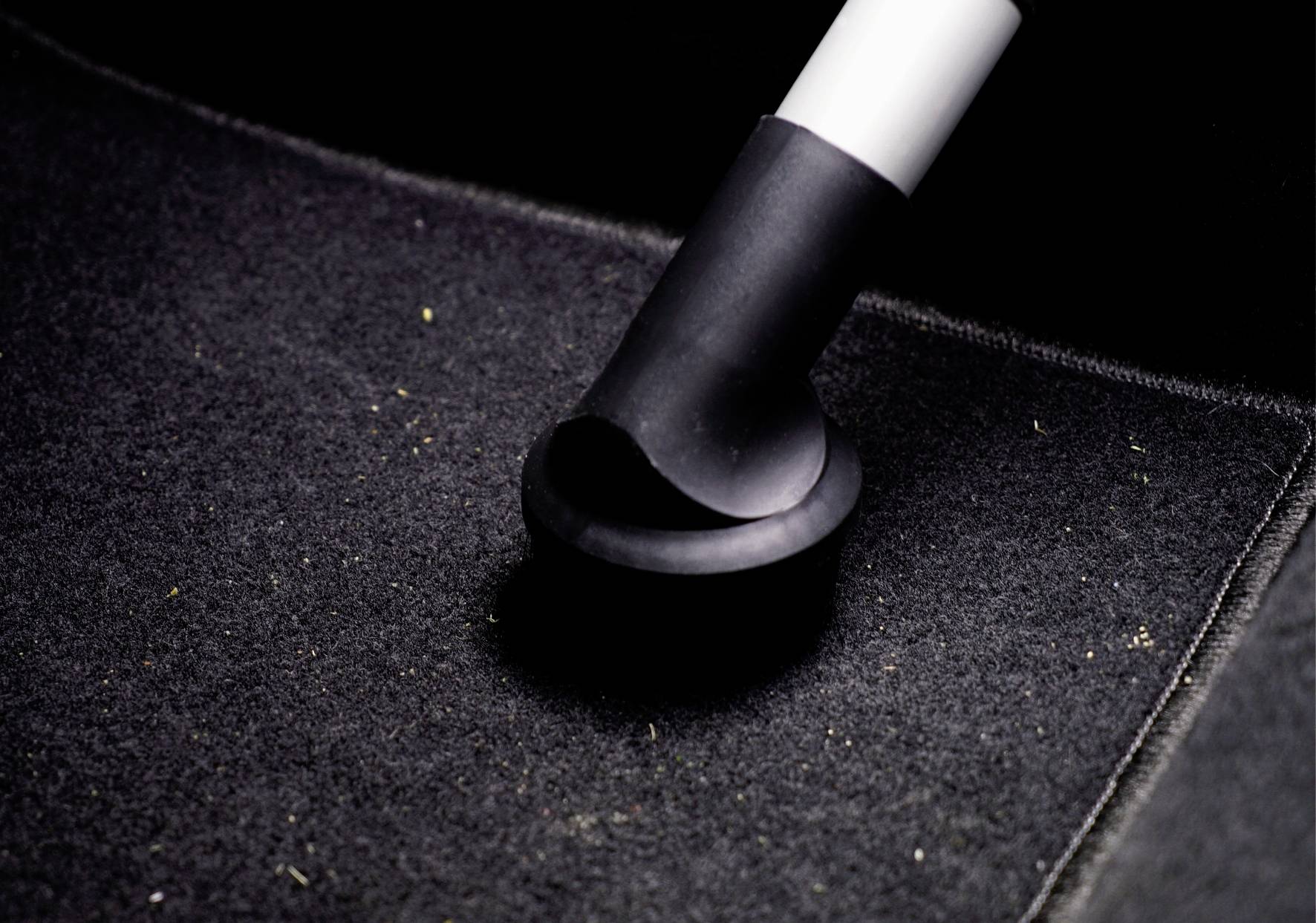 A vacuum cleaner hose is sucking dirt from a black carpet.