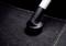 A vacuum cleaner hose is sucking dirt from a black carpet.