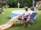 A man is inflating an air mattress on a lounger in the garden. An inflatable pool stands in the background.