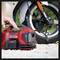 A person is using a portable compressor to inflate a motorcycle tyre. The compressor is red and compact.