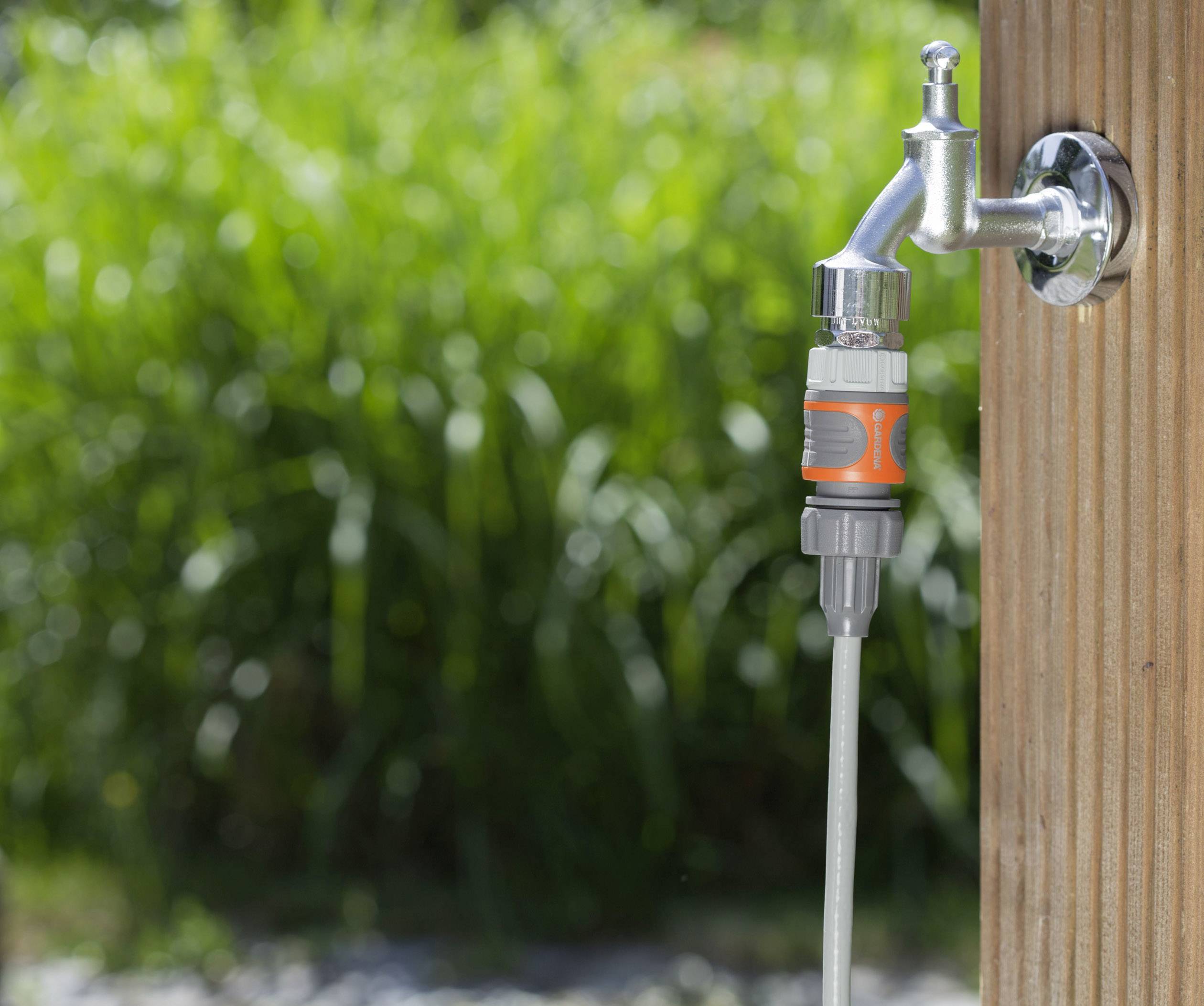 A hosepipe is connected to an outdoor tap, in front of a blurred green background.