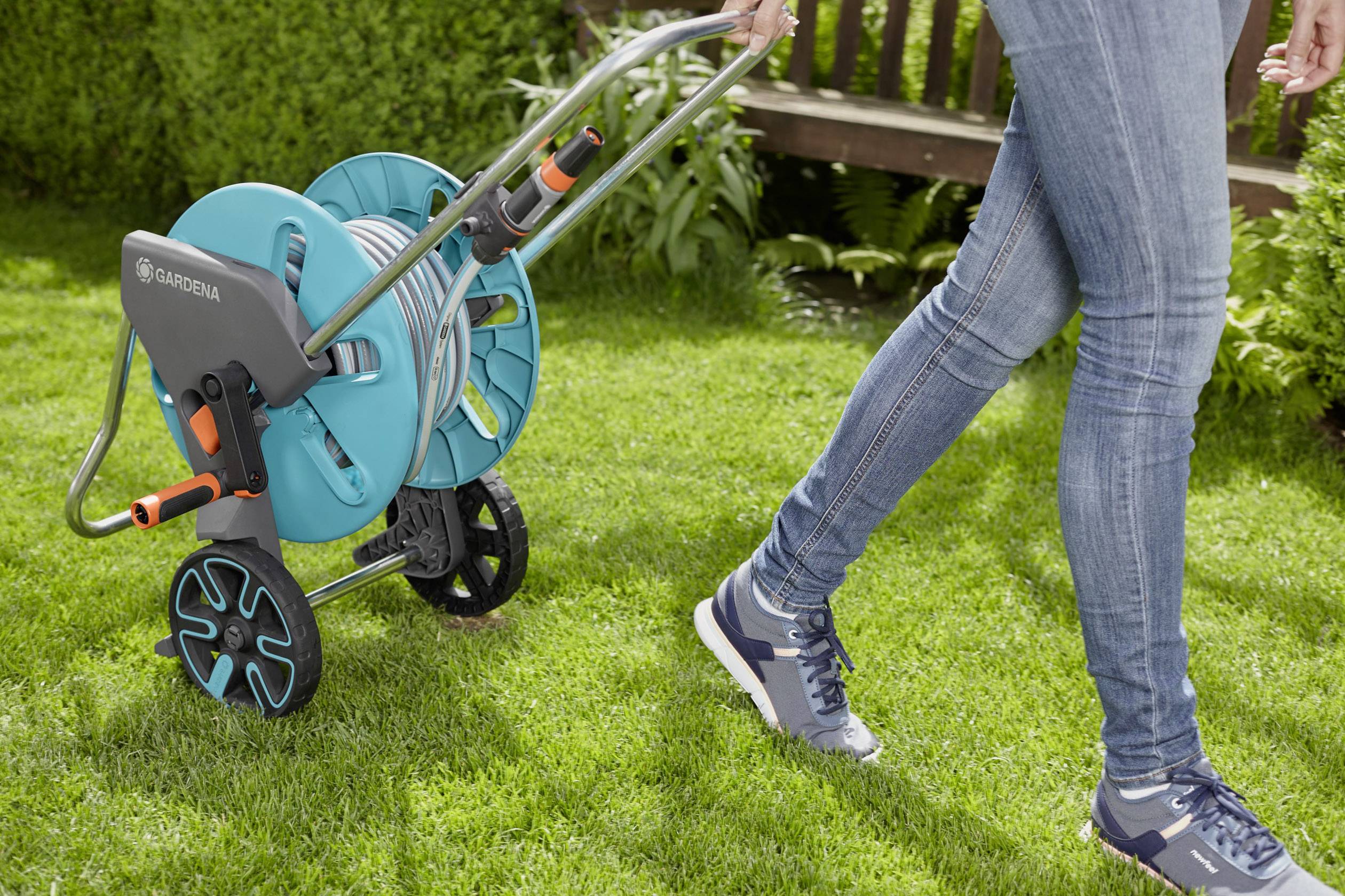A person is pulling a garden hose reel across the lawn. The hose reel is blue and has two wheels for easy movement.