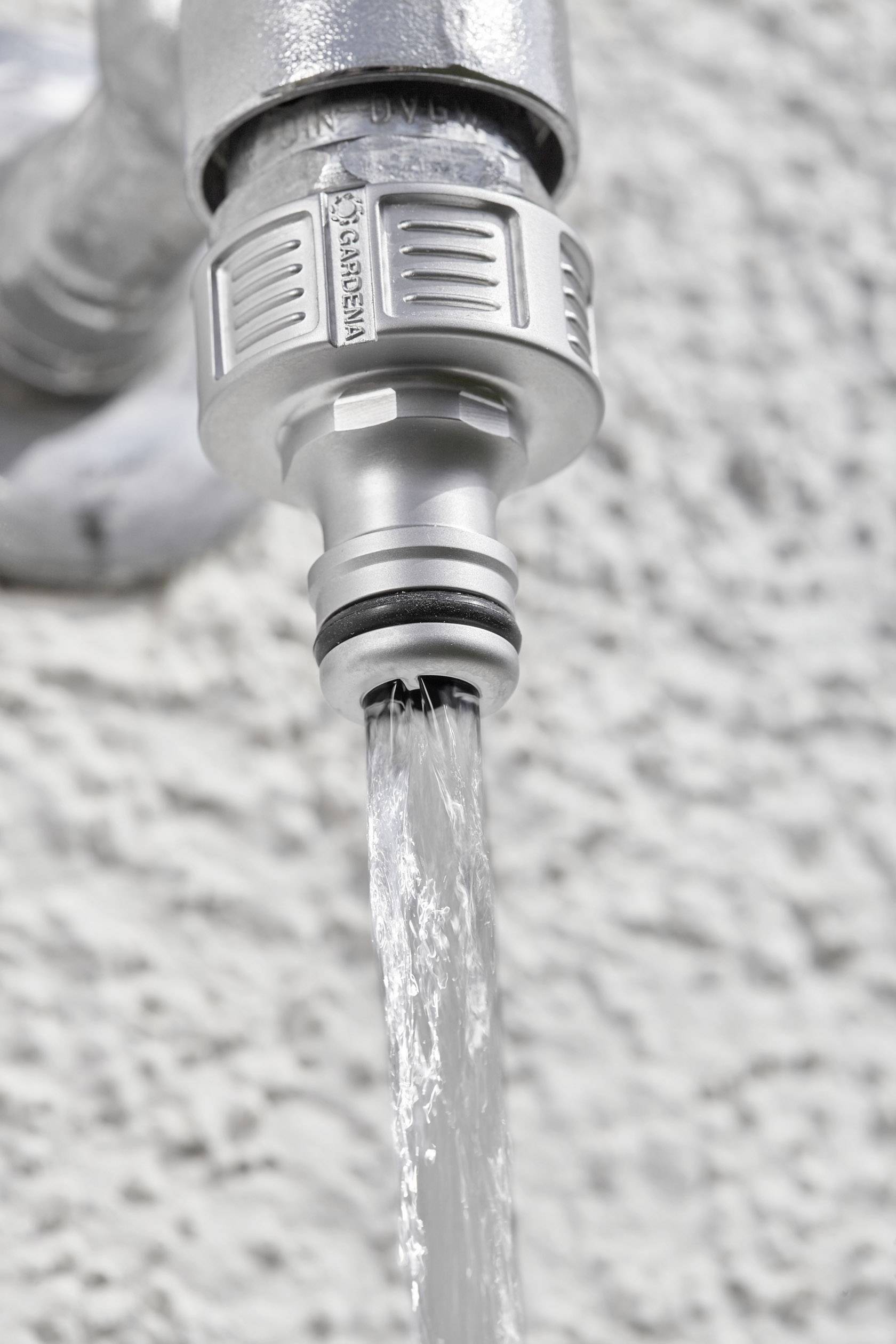 A tap with an attached hose adapter, from which water flows in a steady stream.