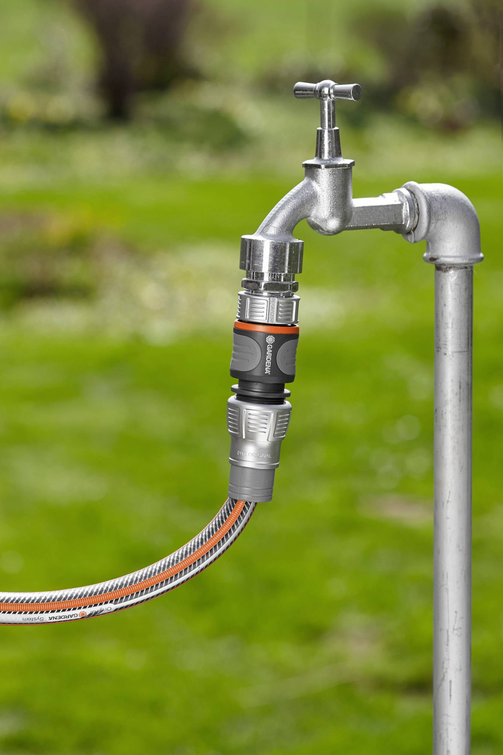 An outdoor tap with a garden hose attached, ready to water a garden in the background.