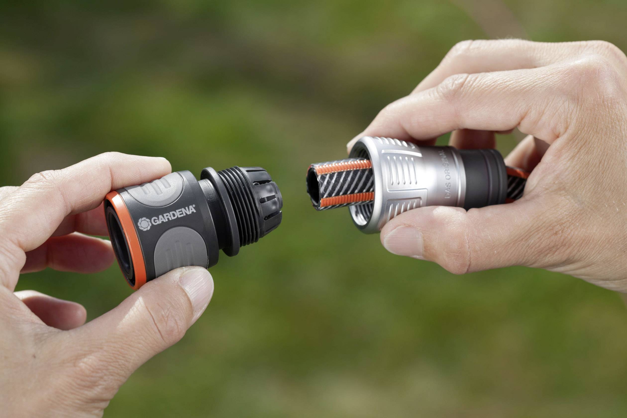 Two hands are holding a Gardena garden hose connector, which is attached to the end of a hose. The background is green.